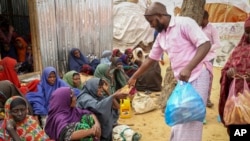 Wasomalia waliotoroka maeneo yanayokumbwa na ukame wakipewa msaada wa chakula , kwenye kambi ya wakimbizi wa ndani, kwenye vitongoji vya Mogadishu, Juni 30, 2022.