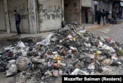 Men stand near garbage filling a street in Aleppo, February 11, 2013. Poor waste management and lack of hygiene have fuelled its spread