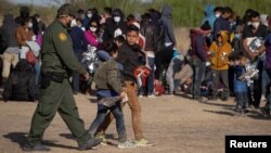 Un agent de la patrouille frontalière américaine escorte deux mineurs non accompagnés alors que d'autres se réfugient près d'un terrain de baseball après avoir traversé le fleuve Rio Grande aux États-Unis depuis le Mexique, sur des radeaux, à La Joya, Texas, le 19 mars 2021.