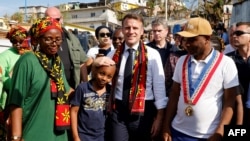 Presiden Prancis Emmanuel Macron (tengah) berjalan bersama sejumlah warga lokal saat berkunjung ke distrik kavani di Mamoudzou, Mayotte, pada 19 Desember 2024, menyusul topan yang memporak-porandakan wilayah tersebut. (Foto: Ludovic Marin/Pool/AFP)