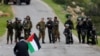 FILE - A demonstrator holds a Palestinian flag in front of Israeli forces as Palestinians protest against President Donald Trump's Mideast initiative, in Jordan Valley in the West Bank, Feb. 25, 2020. 