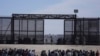 Des migrants qui ont traversé la frontière entre le Mexique et les États-Unis attendent à côté du mur frontalier américain où des agents de la patrouille frontalière américaine montent la garde, vus de Ciudad Juarez, Mexique, le 30 mars 2023.