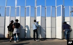 FILE - People peek in the site of the new national stadium, which will host the opening and closing ceremonies and track and field of the 2020 Tokyo Olympics, in Tokyo, Oct. 2, 2016.
