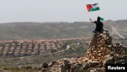 A protester waves a Palestinian flag in front of the Jewish settlement of Ofra during clashes near the West Bank village of Deir Jarir near Ramallah, Apr. 26, 2013.