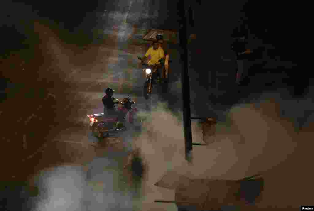 Men on motorcycles look at firefighters extinguishing motorcycles set ablaze by anti-government demonstrators at Altamira Square in Caracas, Feb. 26, 2014.&nbsp;