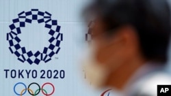Un homme portant un masque facial marche devant un panneau d'affichage avec le logo des Jeux olympiques de Tokyo 2020, à Tokyo, au Japon, le 2 avril 2020. (AP)