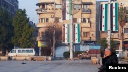 FILE - On Jan. 8, 2025 — about a month after the ouster of Syrian leader Bashar al-Assad — a man sits in Aleppo, Syria, near flags reflecting new leadership. Diplomats from around the world are pushing to stabilize Syria in the wake of Assad's fall. 