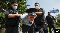 Police officers detains a protester, center, dressed as a Russian police officer before a court hearing of the New Greatness group who are charged with the organization of an extremist association in Moscow, Russia, Aug. 6, 2020.