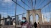 A woman wears a mask as she crosses the Brooklyn Bridge in New York, March 16, 2020. The bridge's pedestrian path is normally crowded on a sunny day.
