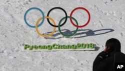 Un homme passe devant les anneaux olympiques avec un signe des Jeux olympiques d'hiver 2018 de Pyeongchang à Pyeongchang, en Corée du Sud, 3 février 2017.