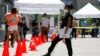 FILE - A medical assistant, right, provides paperwork to people in line at a walk-up COVID-19 testing site in Dallas, Texas, June 11, 2020. 