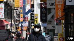一位戴口罩的韩国女性走在首尔购物区街头。